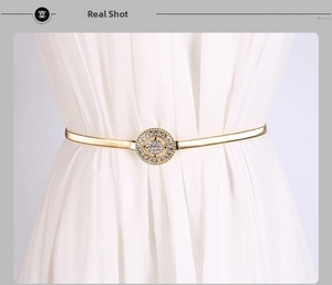 Détail d'une fine ceinture dorée en métal avec boucle ronde en strass sur une robe