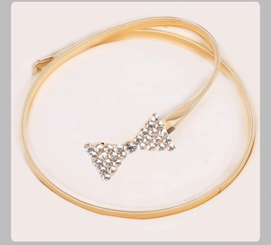 Détail de la ceinture dorée élastique avec une boucle en forme de nœud sertie de strass