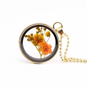 Macro shot of circular gold necklace pendant with preserved orange and yellow dried flowers