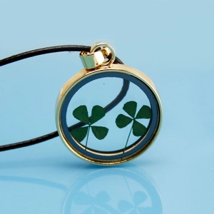 Detailed close-up of a gold circular pendant with two real four-leaf clovers inside