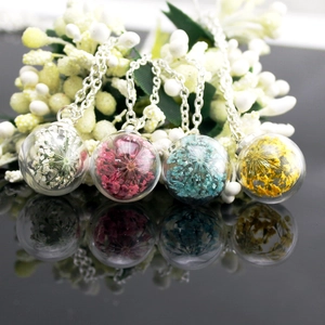Macro detail of four silver-tone necklaces with dried flower glass globe pendants in black