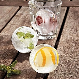 Large spherical ice ball with lemon and mint inside for whiskey on a wooden table