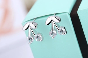 Macro shot of silver cherry stud earrings with clear cubic zirconia on a blue jewelry box