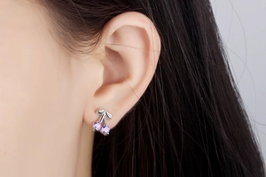 Close-up of cherry stud earring with purple cubic zirconia stones on a model ear