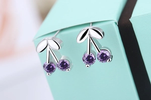 Macro shot of silver cherry earrings with purple zircon stones on a blue gift box