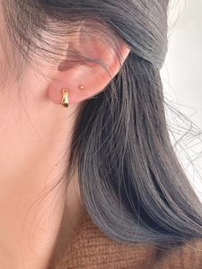 Close-up of polished gold huggie hoop earring paired with a minimalist ball stud earring