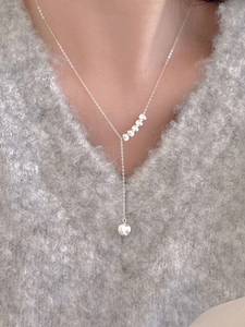 Detail of silver S925 beaded Y-necklace on model wearing a grey V-neck sweater