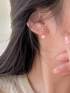 Close-up of elegant bow earrings with heart-shaped shell pendant on model's ear
