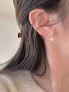 Close-up of S925 silver bow and heart pendant earrings worn on woman's earlobe