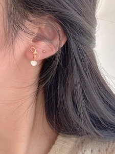Detailed close-up of a 925 sterling silver bow earring with a white heart shell pendant