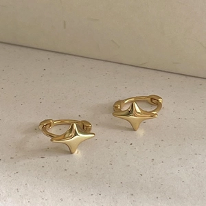 Gros plan d'une boucle d'oreille étoile dorée minimaliste sur fond de pierre beige