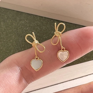 Detailed close-up of gold bow earrings with a heart-shaped mother-of-pearl pendant