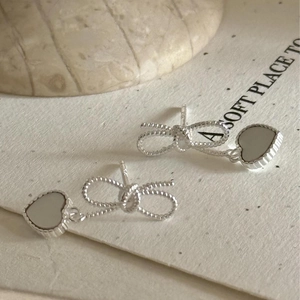 Macro detail of silver bow earrings with heart-shaped white shell inlay and grainy texture