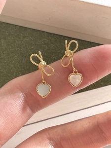 Macro shot of 925 silver bow stud earrings with heart shell pendants in golden finish