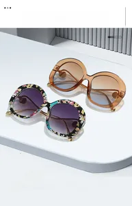 Detail of trendy oval sunglasses with floral and amber frames on a minimalist white stand