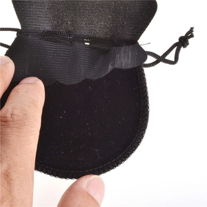 Detailed view of a small black velvet drawstring jewelry pouch being opened by hand