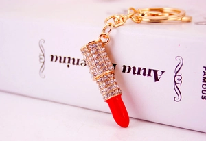Close-up of a gold metal lipstick keychain with red enamel and sparkly rhinestones