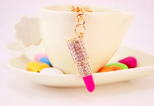 Detail of a sparkling crystal lipstick keychain hanging on a white teacup's edge