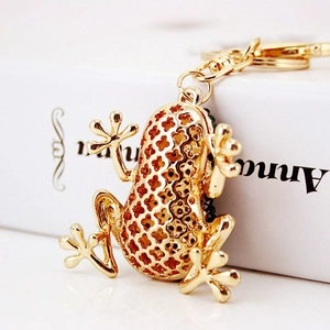Golden frog shaped metal keychain with hollow pattern design on a book background