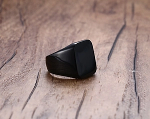 Macro shot of a black minimalist square signet ring for men on a wood surface