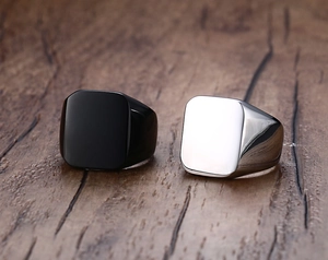 Detail view of silver and black square signet rings on a polished wood surface