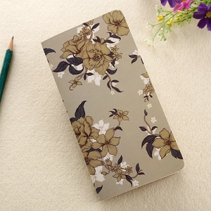 Flat lay of a beige floral kraft paper notebook with a green pencil on a textured surface