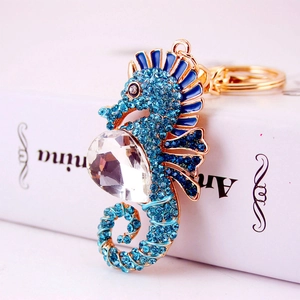 Sparkling blue rhinestone seahorse keychain with golden metal base on a white book