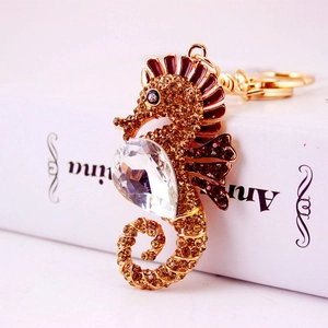 Golden seahorse keychain with brown crystals and enamel on a white book surface