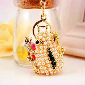 Golden frog keychain with white pearls and green crystals on a floral background