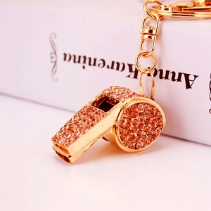Golden whistle keychain with sparkling amber rhinestones on an elegant book background