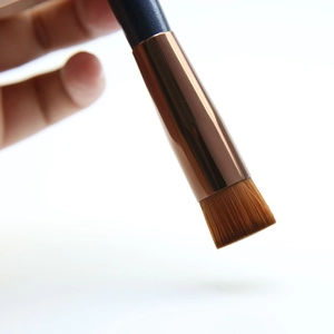 Detailed close-up of a flat-top concealer brush with dense brown bristles and blue handle