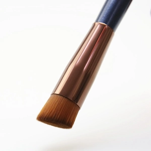 Detail of angled concealer brush with dense brown bristles and a sleek navy blue handle