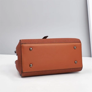 Detailed base of caramel leather handbag featuring silver studs and woven texture