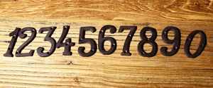Vista dettagliata di numeri civici 0-9 in ghisa con fori per viti su fondo in legno