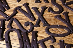 Vista macro di lettere e numeri in ghisa marrone scuro con fori per viti su legno grezzo