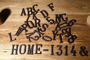 Dettaglio di lettere e numeri in ghisa vintage che formano HOME-1314 su legno rustico