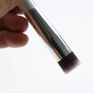 Close-up of small flat-top foundation brush with silver handle and dual-tone bristles
