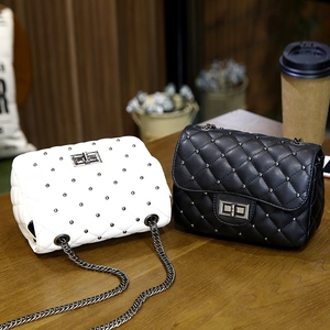 Quilted studded chain bags in black and white leather finish on a wooden tabletop