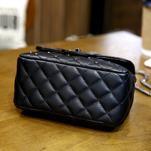 Quilted black leather crossbody bag with silver studs on a wooden table setup