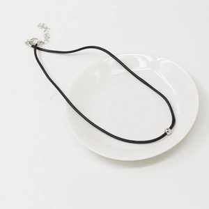 Collier minimaliste en cordon de cuir noir avec perle argentée sur une assiette blanche