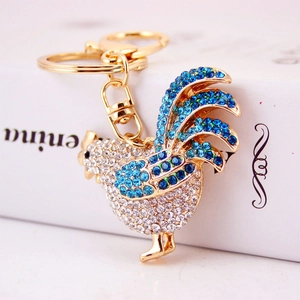 Portachiavi gallo dorato con strass bianchi e blu su una confezione regalo decorata