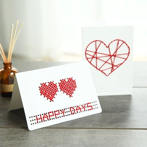 Creative DIY heart cross-stitch greeting card on rustic wooden desk with soft light