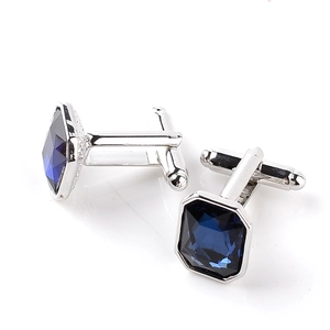 Macro detail of silver cufflinks with square-cut navy blue crystal stones on white background