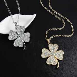 Close-up of gold and silver four-leaf clover crystal pendants on a black textured background