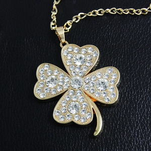 Macro shot of gold clover pendant necklace featuring sparkling pavé crystals on black leather