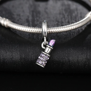 Macro detail of a silver lipstick charm with purple rhinestones on a beaded bracelet