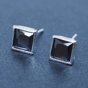 Macro view of square 925 silver stud earrings with black zircon stones on a textured surface
