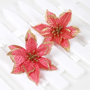 Close-up of artificial red Christmas flowers with gold glitter edges on white fence