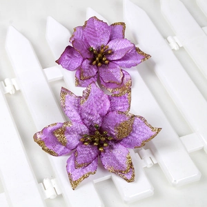 Close-up of purple artificial Christmas flowers with gold glitter edges on white fence