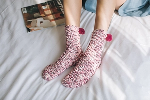 Detail of pink coral fleece socks with cute pom-poms worn in a cozy home setting